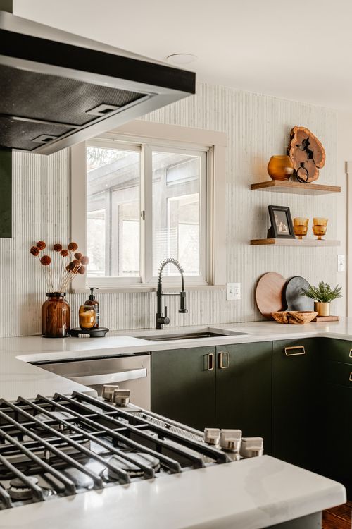 Kitchen range hood over a gas cooktop beside a window and decorative floating shelves