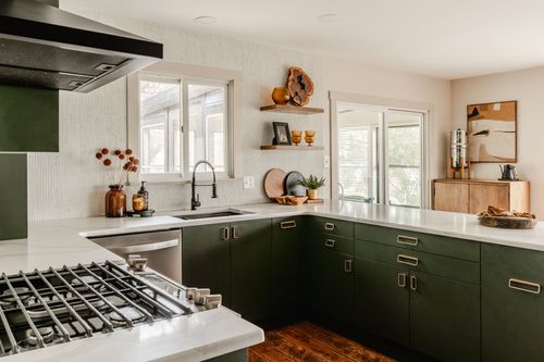 Kitchen corner with green cabinetry, gas range, sink and open shelving with decor