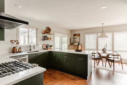 Open-plan kitchen with green cabinets and a gas range with a dining area beyond