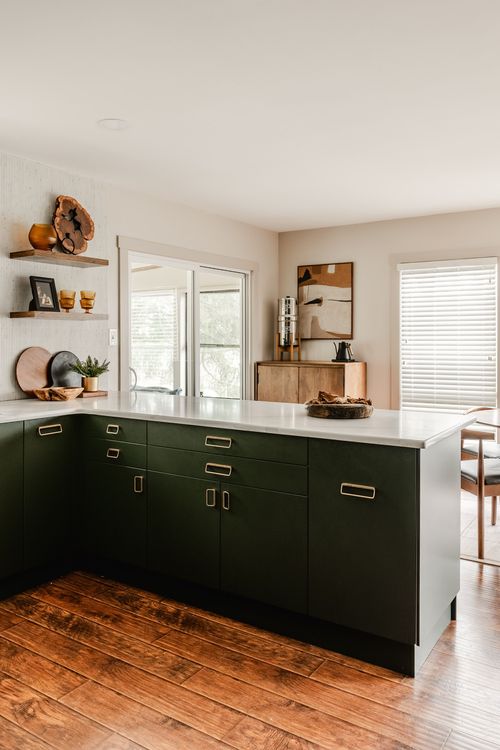 Kitchen island with green cabinetry, brass pulls and wood flooring near a sliding door