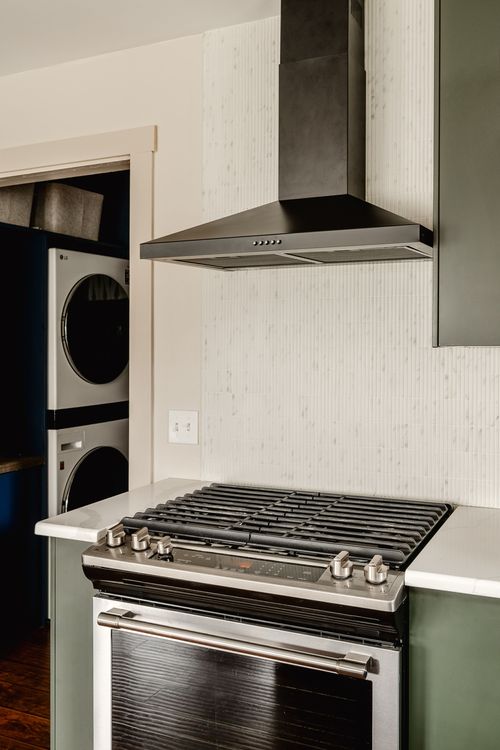 Range hood over a gas cooktop beside a stacked washer and dryer nook