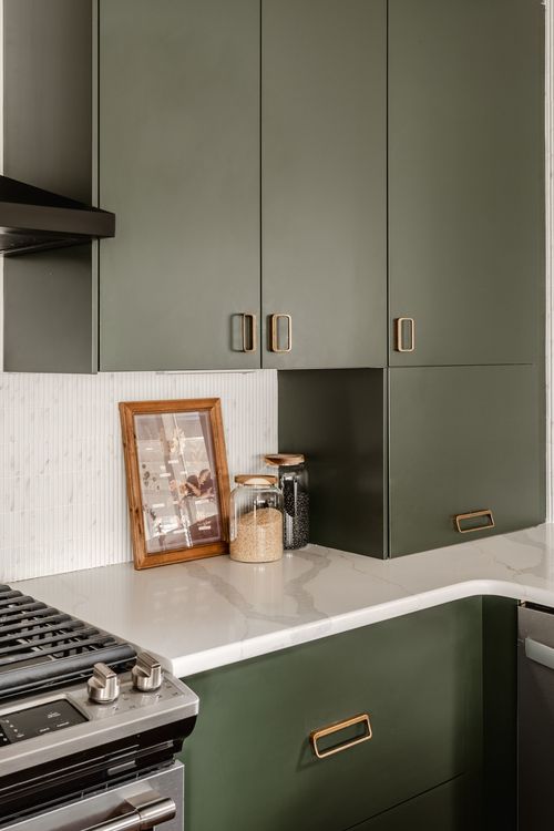Close-up of green upper cabinets with brass pulls above a marble countertop