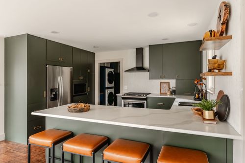Open kitchen with green cabinetry, a stainless refrigerator and leather counter stools