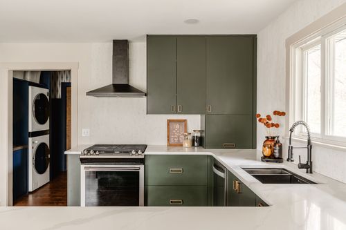 Kitchen with green cabinets and a range hood beside a view into a laundry nook