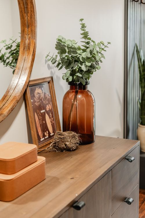 Close-up of a framed botanical print, amber glass vase and dried nest on a console table