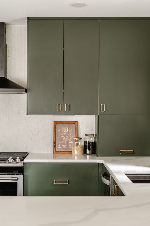 Close-up of olive green kitchen cabinets with brass hardware and a white quartz countertop