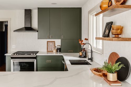 Kitchen island with white quartz counter, green cabinetry and black range hood