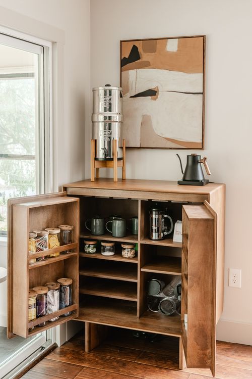 Wood coffee bar cabinet open to reveal mugs, glassware and coffee supplies