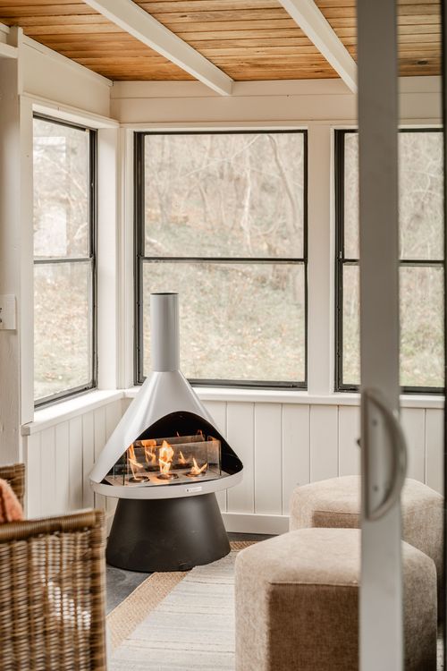 Screened porch with a freestanding conical fireplace, wicker basket and wood plank ceiling