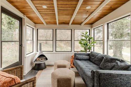 Sunroom with wood beam ceiling, gray sofa, modern fireplace and large screened windows