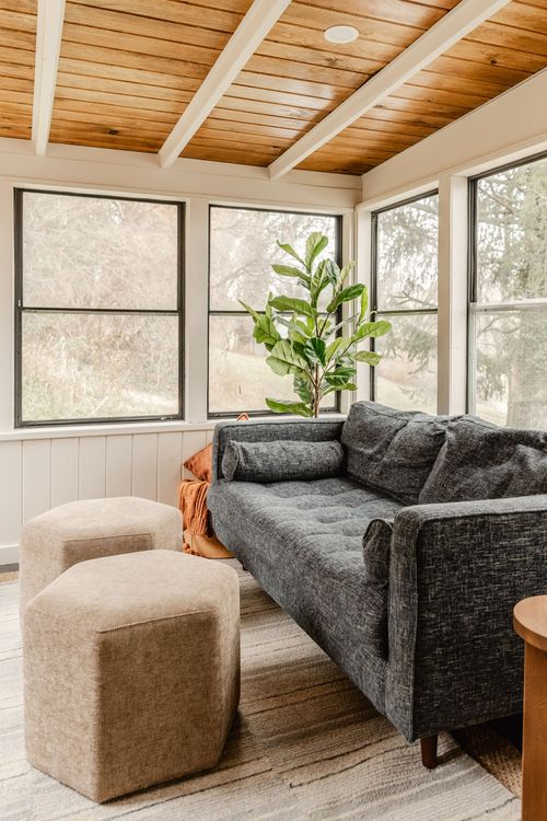 Sunroom seating area with gray sofa, tan poufs and a fiddle leaf fig by the windows