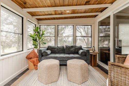 Sunroom with gray sofa, woven armchair and layered tan poufs on a jute rug