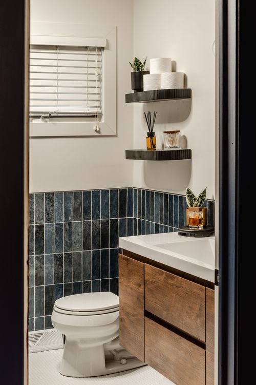 Powder room with navy tile wainscoting, wood vanity and floating black shelves