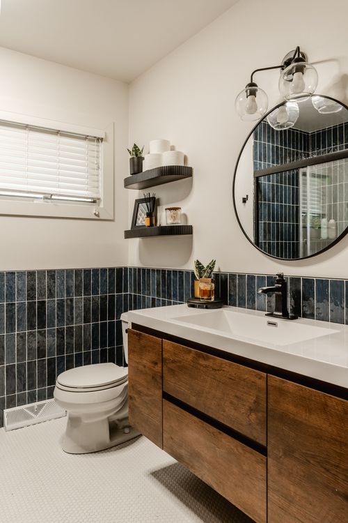 Bathroom with round black-framed mirror, navy tile backsplash and walnut vanity