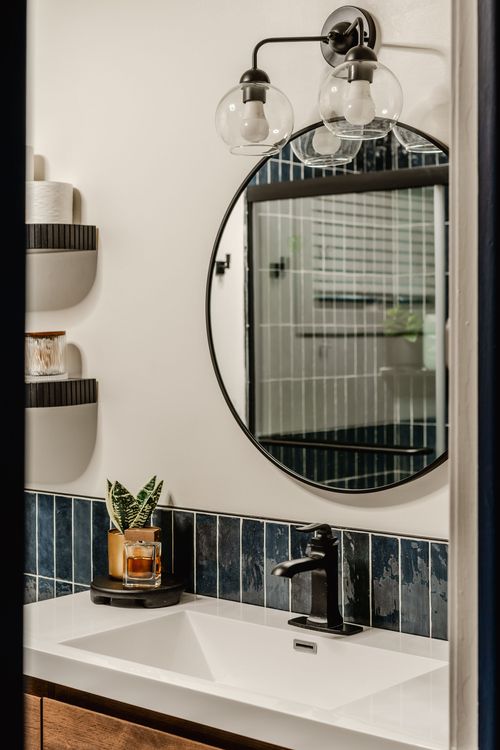 Close-up of a round black mirror and glass globe sconce over navy tile