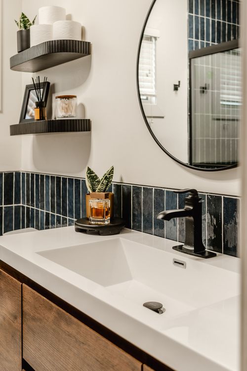 White vanity sink with black faucet, navy tile backsplash and round mirror
