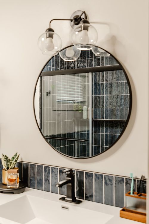 Round black-framed mirror with glass globe sconce reflecting the bathroom