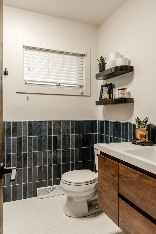 Powder room with navy tile wainscoting, toilet and floating black shelves