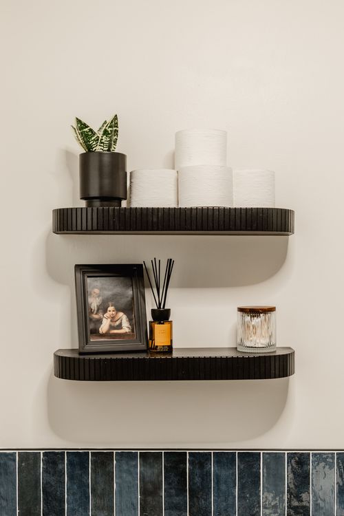 Floating black shelves holding towels, a framed portrait and a reed diffuser