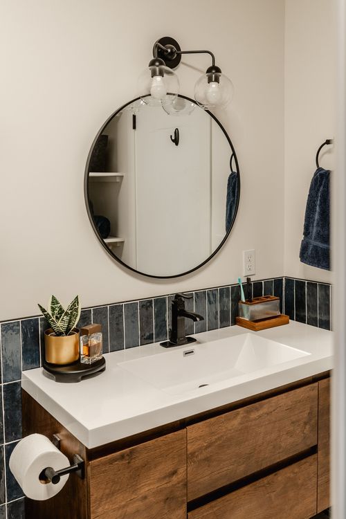Bathroom vanity with round mirror, black sconce, navy tile and walnut cabinetry