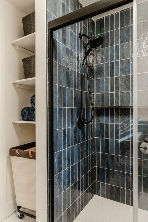 Close-up of a black handheld shower fixture against navy zellige-style tile