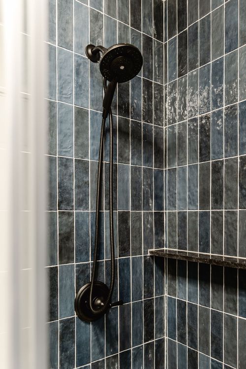 Glass shower enclosure with navy tile, black fixtures and a built-in niche shelf