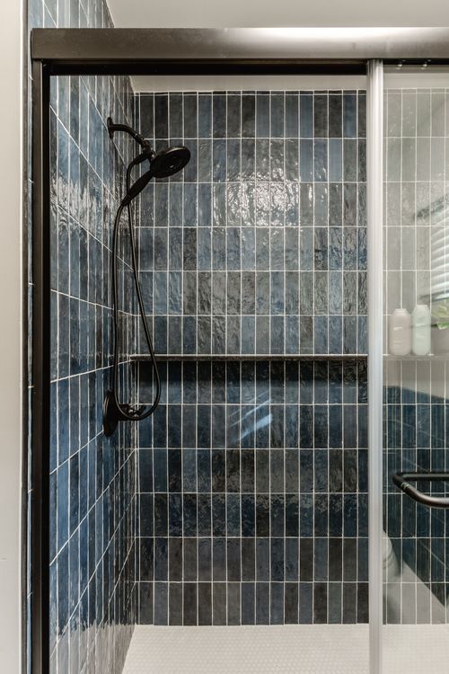 Corner shower niche with navy tile shelf holding shampoo bottles and a small plant