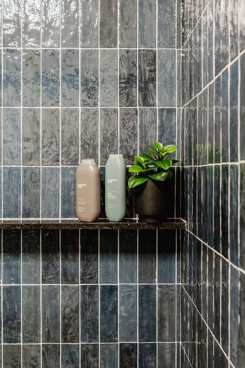 Shower with dark blue tile and a black handheld sprayer beside a built-in shelf
