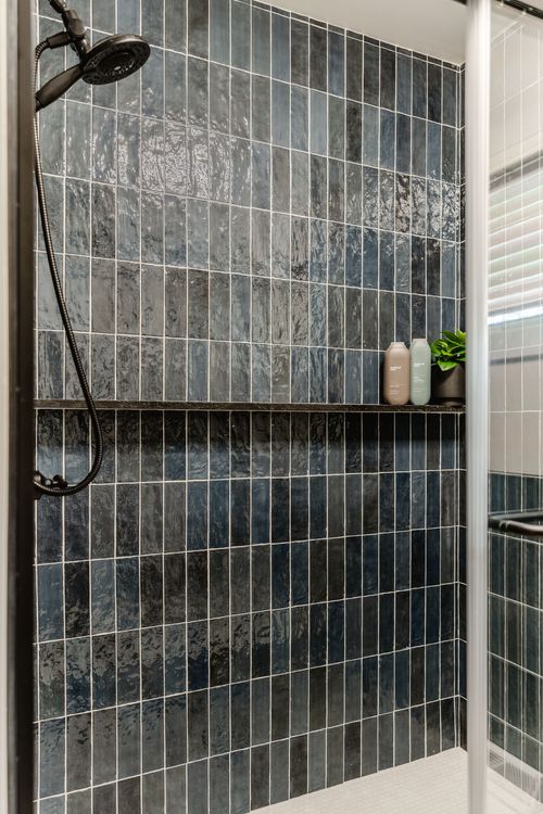 Glass-enclosed shower with navy tile, black fixtures and a tiled bench niche