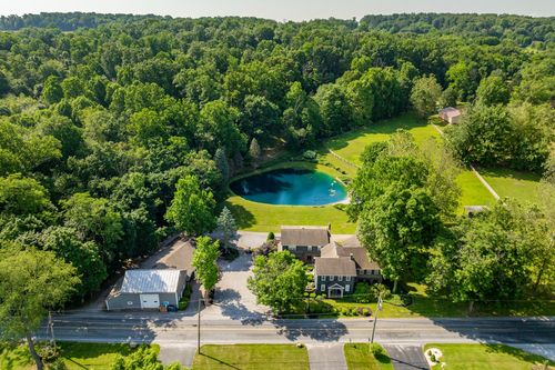 Aerial view of a large home with covered porches beside a wooded pond and open lawn