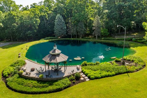 Aerial view of an emerald-green pond with a stone-patio gazebo and fountain surrounded by trees