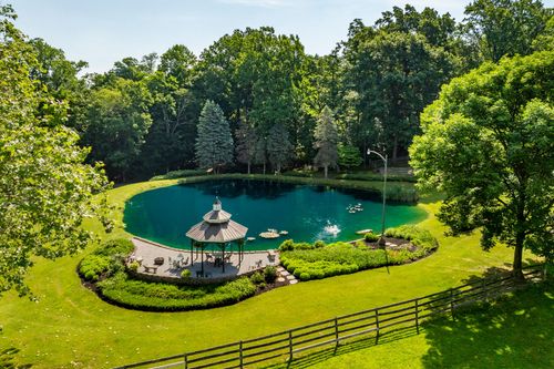 Aerial view of a private pond with a wood gazebo, curved paver patio and split-rail fencing