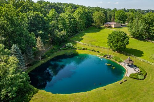 Aerial view of a pond with a fountain, gazebo and split-rail fence beside a large lawn