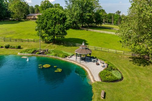 Aerial view of a pond-side gazebo with paver patio, lily pads and split-rail fencing