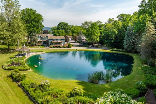 Aerial view of a house beside a pond with lily pads, a gazebo and flowering landscape beds