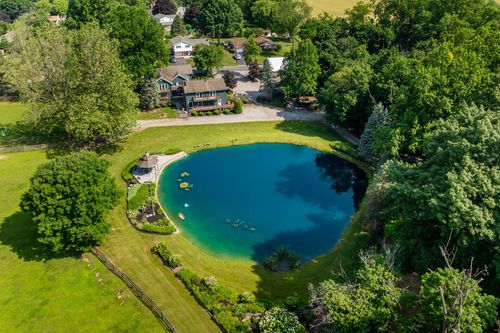 Aerial view of a wooded property with a private pond surrounded by farmland and neighboring homes