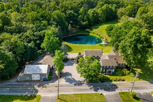 Aerial view of a large home with a gazebo by the pond and a circular driveway
