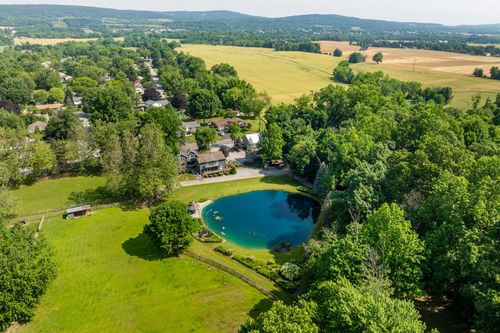 Wide aerial view of a rural property with a pond tucked among trees near open farm fields