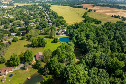 Aerial view of a tree-lined pond bordered by farmland with distant hills on the horizon