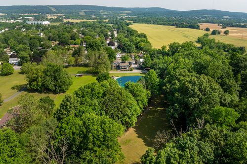 Aerial view of a wooded pond nestled among trees with rolling hills in the distance