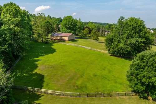 Aerial view of a detached barn with a metal roof beside a fenced grassy pasture