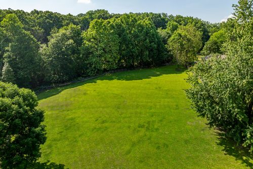 Aerial view of an open grassy lawn bordered by mature trees and a wood fence
