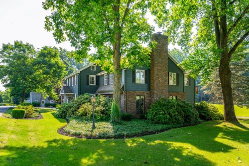 Blue-gray colonial home with a stone chimney, brick accents and manicured landscaping