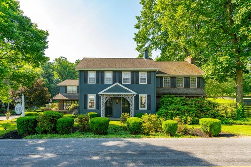 Blue-gray colonial farmhouse with a wraparound porch, twin chimneys and mature shade trees