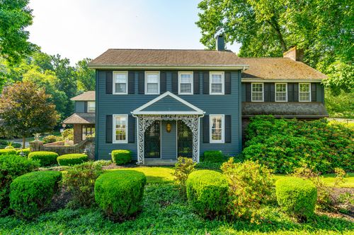 Front exterior of a blue-gray colonial home with an ornate white porch entry and manicured hedges