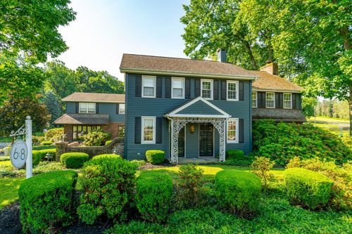 Two-story colonial home with black shutters, a decorative porch and neatly trimmed hedges