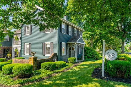 Blue-gray colonial home with a Victorian iron porch entry and brick planter beside the driveway