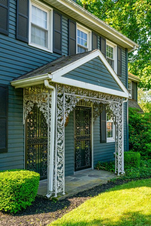 Close-up of an ornate white ironwork porch entry on a blue-gray colonial home
