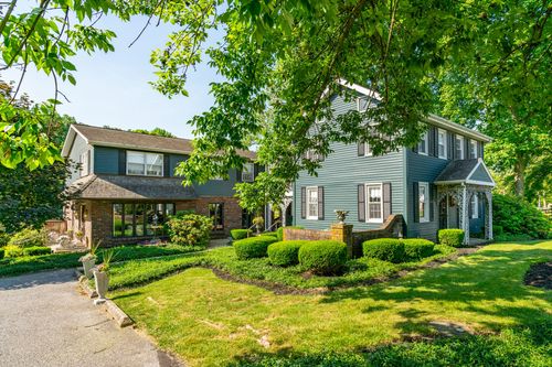 Large colonial home combining brick and blue-gray siding with black shutters and mature landscaping