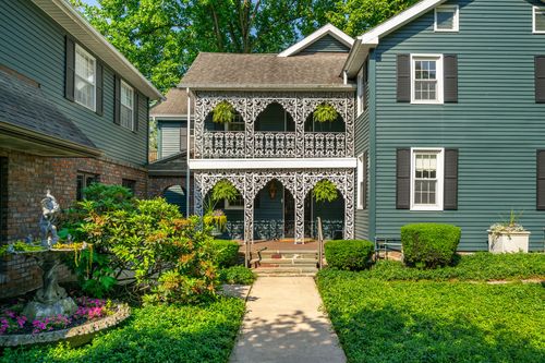 Two-story ornate white ironwork porch with hanging ferns on a blue-gray colonial
